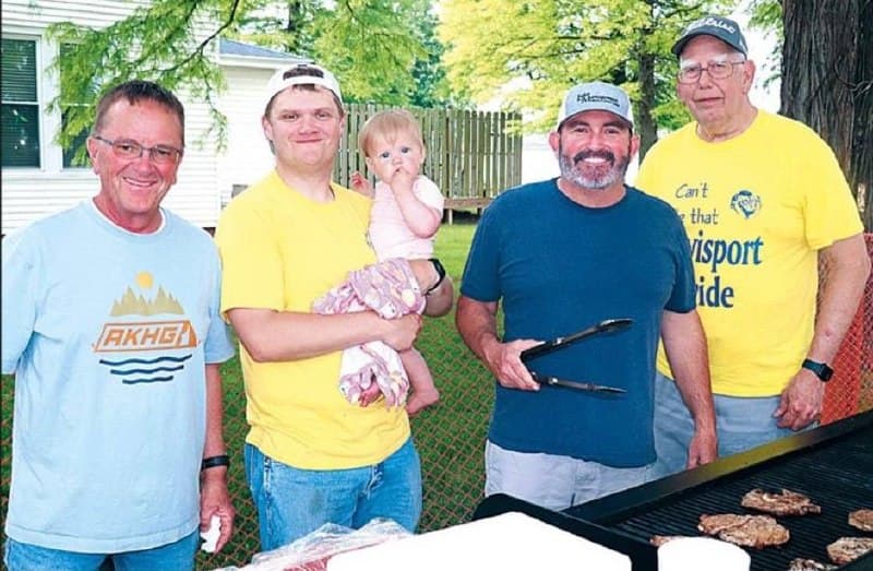 Lions Club volunteers and family gathered around a grill outdoors during a community cookout.
